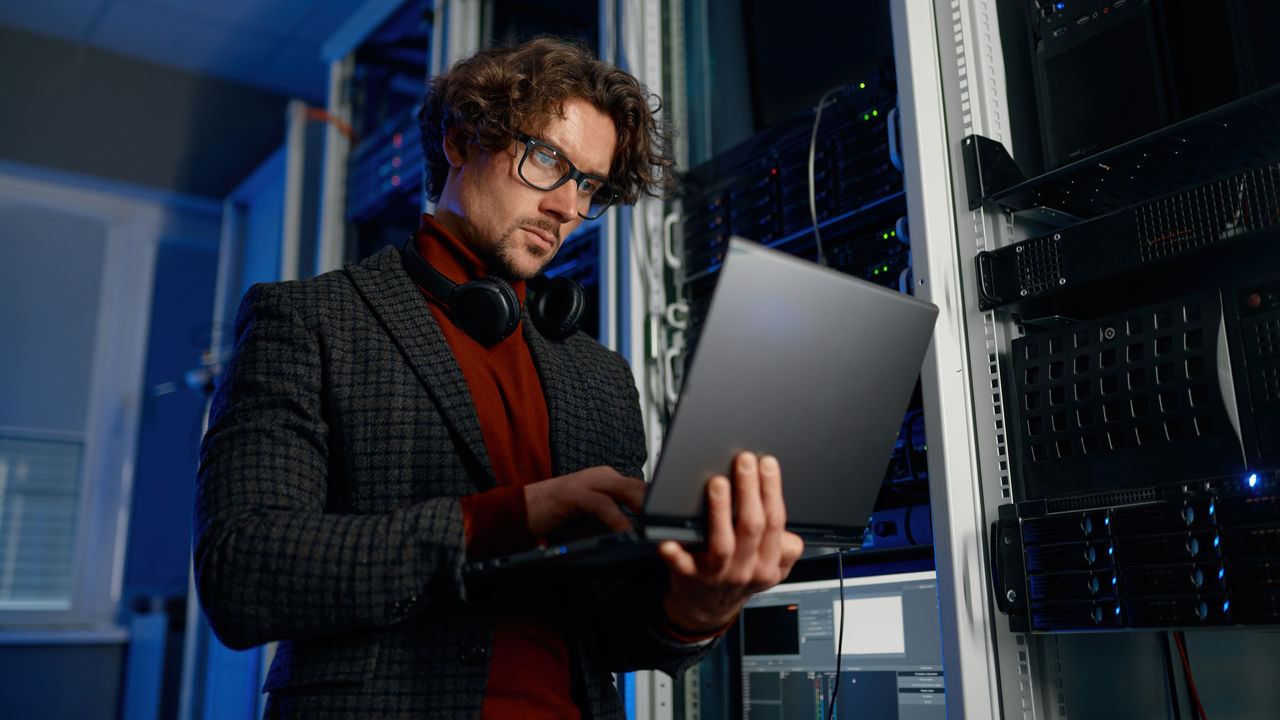 IT technician using digital tablet while working in data center with server rack. Smart technology system administration