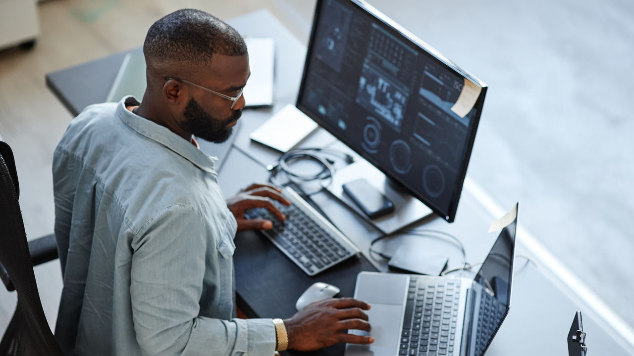 Minimal high angle view at African American software developer working with computers and data systems in office