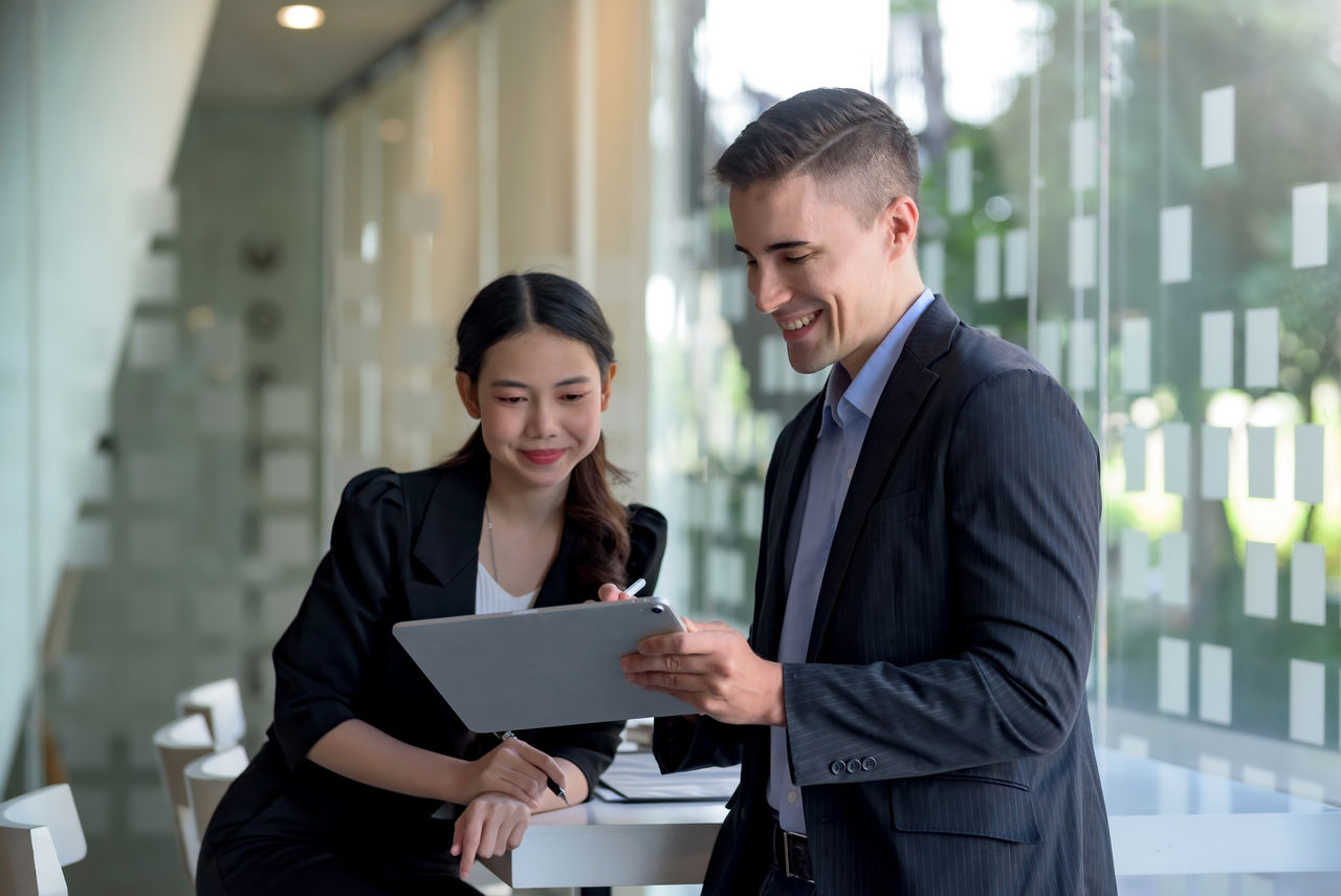 Two business people discuss investment project working and planning strategy. Businessman and businesswoman talking together with tablet at office.