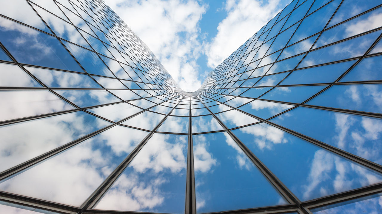 Blue sky and white clouds reflecting in a curved glass building
