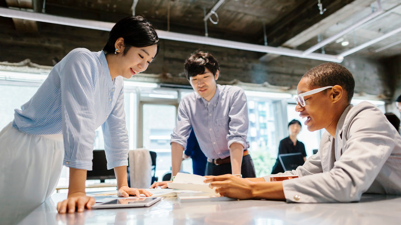 A group of multi-ethnic young business people are talking to each other in a modern working space in Tokyo.