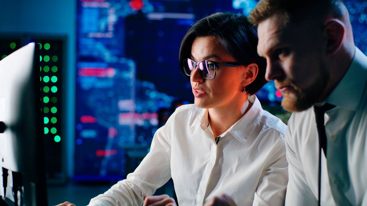 Man and woman browsing and discussing data on computer while working together in high tech digital security center